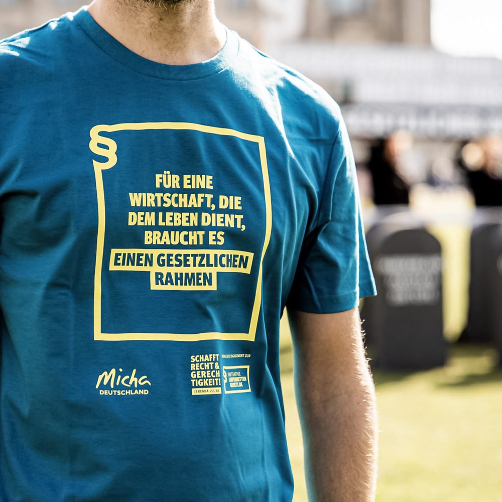 Mann trängt Micha-T-Shirt zur Kampagne Lieferkettengesetzt. Aufdruck: Für eine Wirtschaft, die dem Leben dient, braucht es einen gesetzlichen Rahmen.
